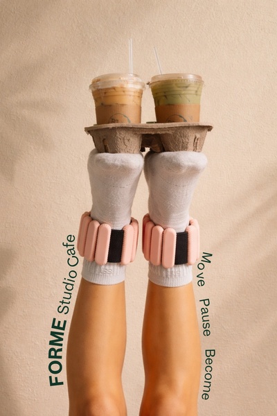 This ad creative features a pair of legs wearing pink ankle weights while balancing a tray of coffee, demonstrating the product's integration into daily life.